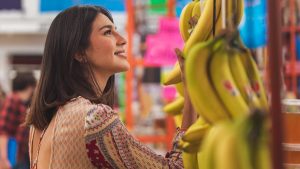 A smiling woman selecting ripe bananas at a lively fruit market.
